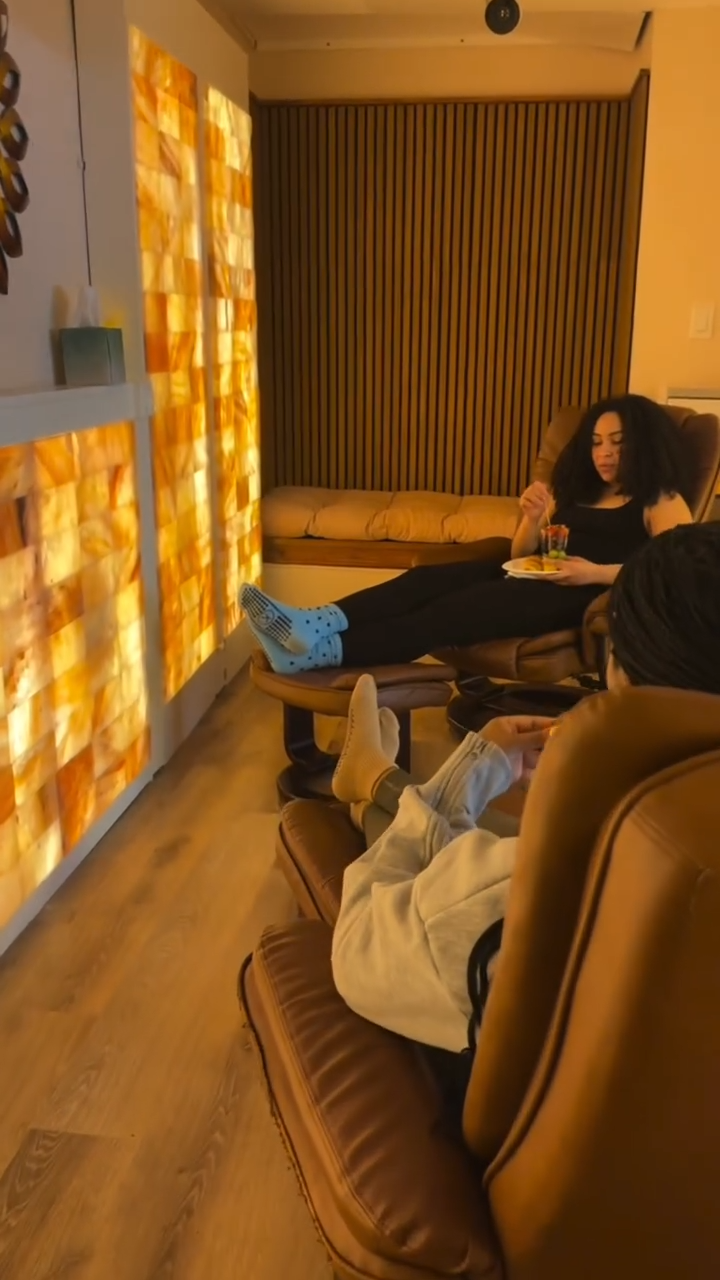 Woman reclining in a leather chair inside a salt-room recovery space with warm orange salt-wall glow