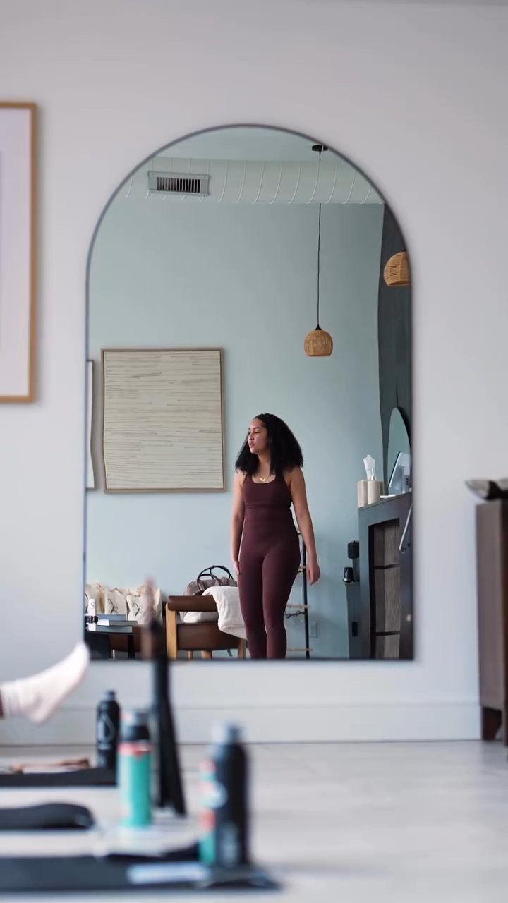 Chantel Monegro in maroon activewear standing in front of an arched mirror in a wellness studio